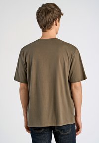Camiseta de algodón de manga corta en verde oliva, con cuello redondo, corte relajado y diseño de hombros sin costuras, exhibida desde la parte trasera.