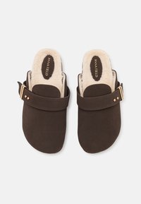 Brune semsket tøfler med en myk, kremfarget fôr og en enkelt spenne. Rund tådesign med flat såle. Gulldetaljer som aksent.