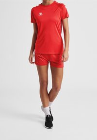 Punainen urheilupaita ja shortsit, valmistettu kevyestä kankaasta, joissa on pyöreä pääntie, lyhyet hihat ja rintataskussa logo.