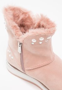 Bottine en daim rose avec doublure en fausse fourrure, fermeture éclair, et ornements en strass le long des côtés et du col. Accent argenté sur la semelle.
