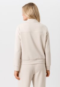 Beige sweatshirt met een hoge kraag en geribbelde manchetten. Soepele textuur en een eenvoudig ontwerp met een horizontale naaddetail op de rug.