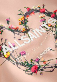 Svetloružová látka s kvetinovou výšivkou v žiarivých farbách okolo textu „ALLSAINTS“ s ďalším textom v japončine a nápisom „LONDON“ pod ním.