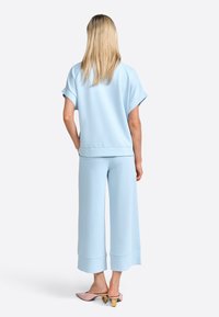 Ljusblått lounge-set som består av en kortärmad topp och byxor med vida ben och kort nederkant. Slät tyge med subtil struktur. Högklackade sandaler.