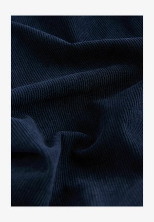Marineblå ribbet stof med en tekstureret overflade, der viser bløde folder og bølger, hvilket fremhæver dets blødhed og dybde.