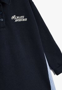Marinblå långärmad polo med "ALWAYS AWESOME" i vit brodyr. Inkluderar ett mönstrat blått och vitt randigt innerfoder.