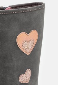 Botte grise avec des appliqués en forme de cœurs roses et pailletés, avec des coutures contrastantes et une finition texturée lisse.