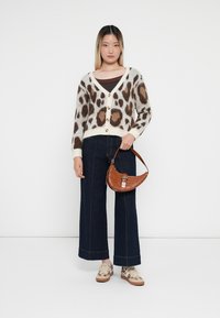 Crème cardigan met bruin luipaardprint, met knoopsluitingen, gecombineerd met donkere wijde been jeans en een bruine crossbody tas. Casual schoenen zichtbaar.