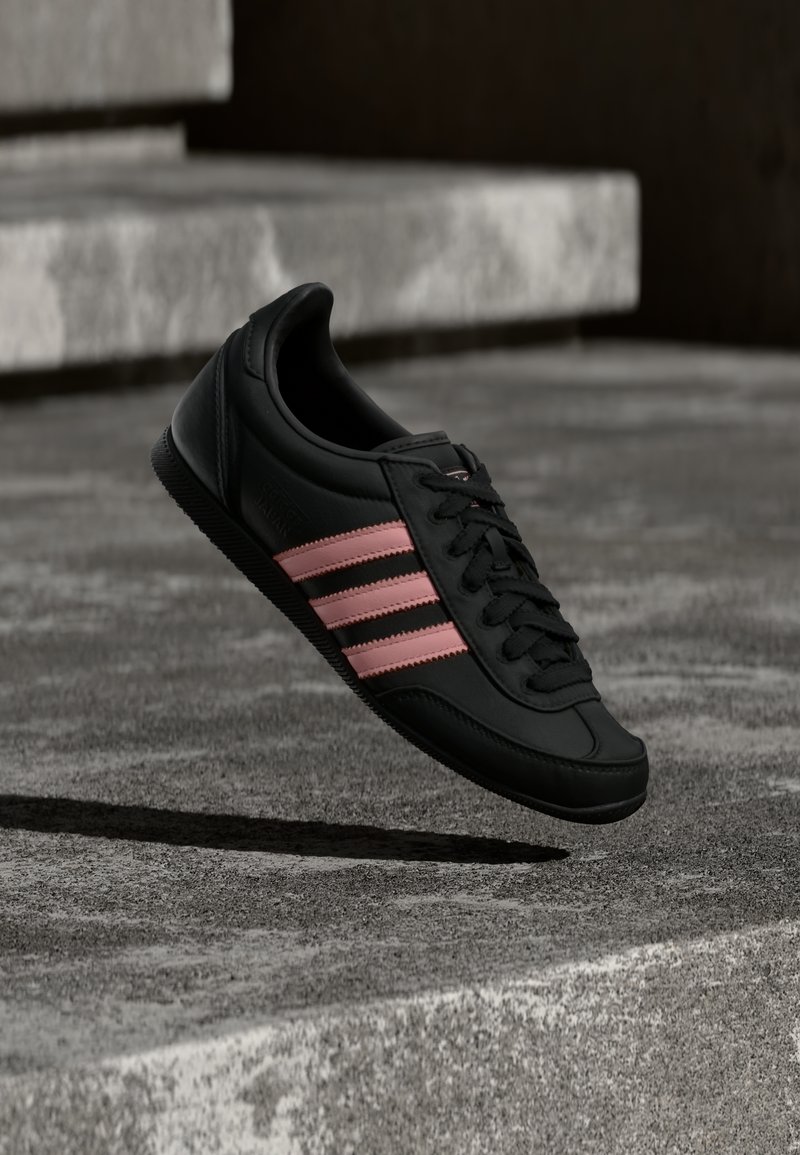 Μαύρο αθλητικό παπούτσι με ροζ ρίγες κρεμασμένο πάνω από τσιμεντένια σκαλοπάτια, ρίχνοντας σκιά στο έδαφος από κάτω.