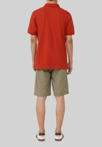 Rode polo met kraag, gecombineerd met lichte khaki korte broek. De korte broek heeft een elastische tailleband. De schoenen zijn wit met zwarte accenten.