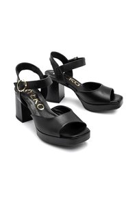 Sandales à plateforme ouvertes en cuir noir avec un talon carré, dotées d'une sangle de cheville réglable et d'un détail de boucle dorée. Texture lisse.