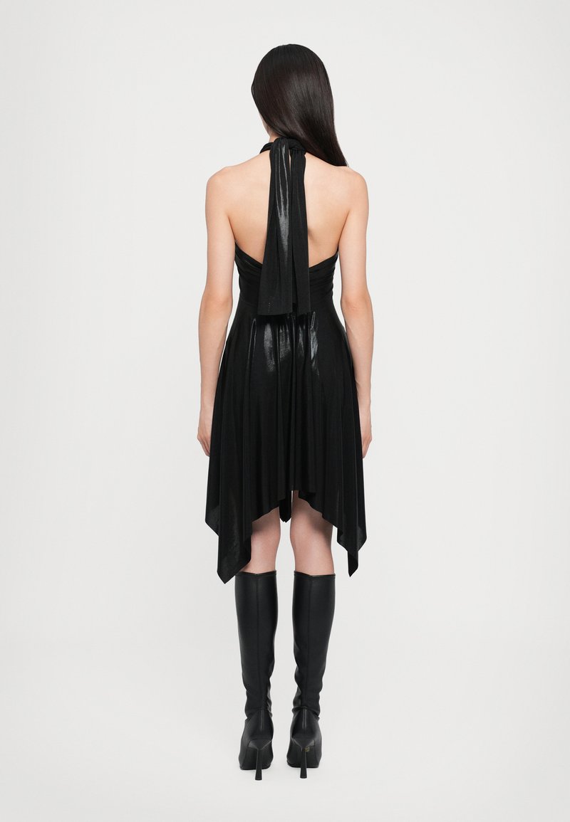 Vestido negro de halter con un cuerpo fruncido y dobladillo asimétrico, que presenta una textura suave y un caída fluida. Combinado con botas negras hasta la rodilla.