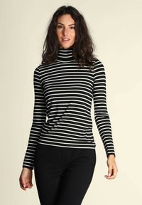 Dolcevita a righe bianche e nere con maniche lunghe, design aderente, texture morbida e collo alto, abbinato a pantaloni neri.