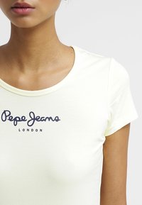 Žluté tričko s krátkým rukávem vyrobené z měkké látky, s námořnickým tištěným logem "Pepe Jeans LONDON" na oblasti hrudníku.