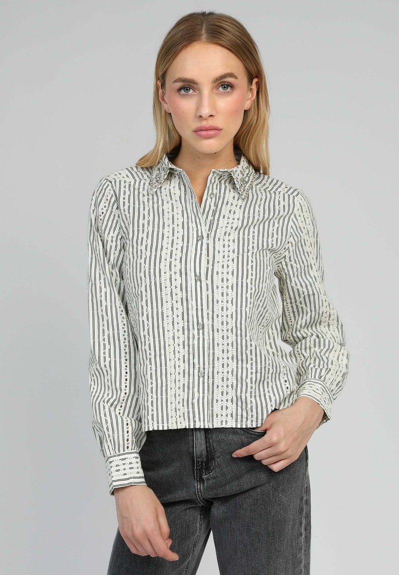 Chemise à boutons avec un motif rayé vertical blanc et noir, dotée d'un col, de manches longues et de détails décoratifs le long des bords.