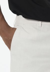 Hellfarbene Hosen aus strukturiertem Stoff mit Seitentaschen und einem genähten Bund, kombiniert mit einem schwarzen Oberteil.