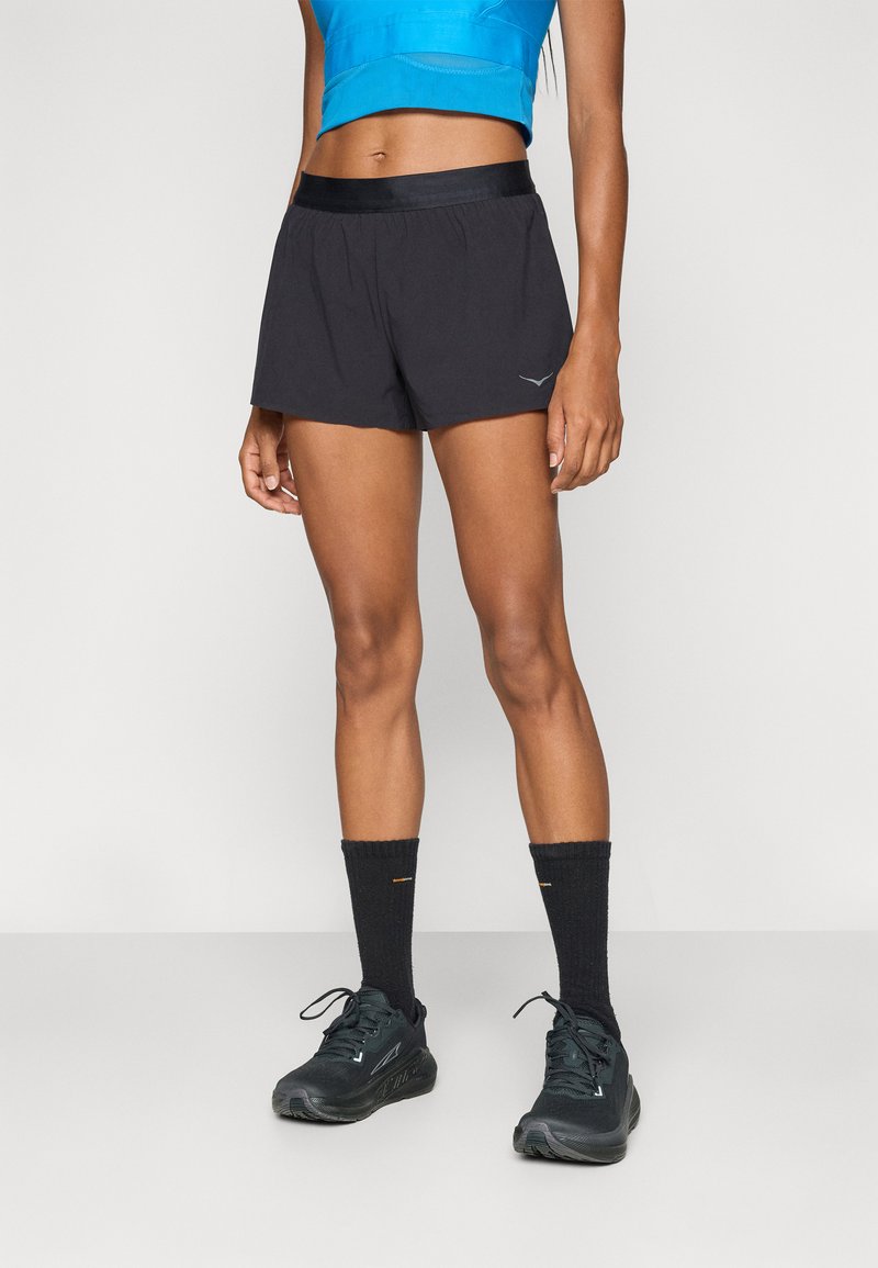 Svarte løpeshorts med elastisk liv, laget av lett stoff. Brukt med svarte sokker og joggesko.