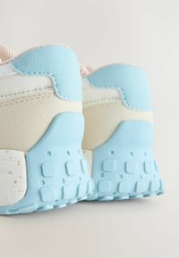 Weißer Sneaker mit hellblauen Akzenten, ausgestattet mit einer strukturierten Hinterferse, glatten Seiten und einem klar definierten Grip-Muster auf der Sohle.