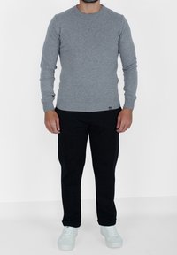 Szary sweter z długim rękawem i okrągłym dekoltem, w parze z czarnymi, zwężanymi spodniami oraz jasnoniebieskimi trampkami. Gładka tekstura, minimalistyczne detale.