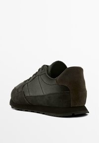 Černá atletická bota s texturovaným koženým svrškem a semišovými akcenty. Design zahrnuje polstrovanou patu a gumovou podrážku.