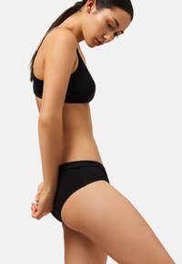 Sujetador de algodón negro y bragas a juego con textura suave. Las bragas presentan un diseño sencillo y un borde de encaje a lo largo de la cintura.