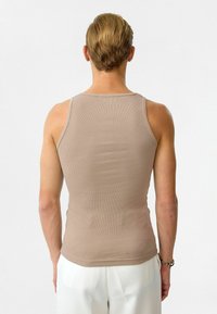 Beige geribbeld tanktop met een nauwsluitende silhouet. Voorzien van een geribbelde textuur en smalle banden, gecombineerd met witte, geplooide broek.