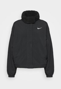 Svart jacka med hög, fleecefoder krage. Tillverkad av smidig tyg, med dragkedja fram, elastiska ärmslut och en liten vit logotyp på bröstet.