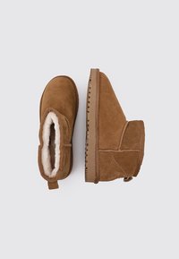 Botines de ante marrón con forro de piel de oveja, punta redondeada, suela de goma texturizada y lengüeta trasera para facilitar el calzado.