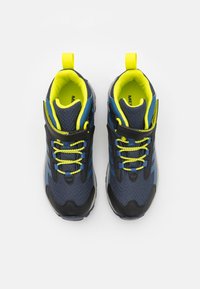 Zapatillas deportivas de color azul marino con parte superior de malla, acentos negros y cordones amarillos brillantes. Presenta un collar acolchado y una lengüeta en el talón.