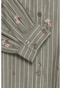 Camisa a rayas verdes con bordados florales en rosa, puños abotonados y una tela suave y texturizada. Detalle de dos botones en el puño.