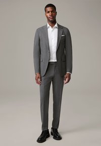 Grijze suit met een gestructureerde afwerking, met een getailleerde pasvorm, witte overhemd en zwarte schoenen. Opvallende details zijn een pochet.