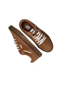 Zapatillas de ante marrón con cordones blancos. Presentan un diseño clásico de corte bajo y una suela de goma. Logo mostrado en el costado y en la lengua.