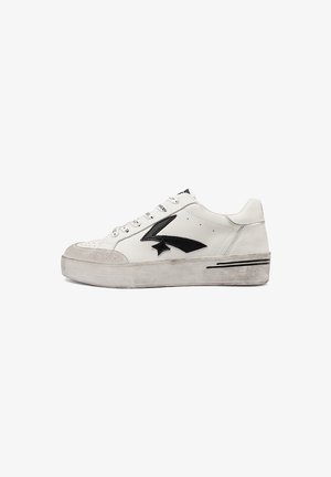 Zapatilla blanca de corte bajo con logo de flecha negra, cierre de cordones, puntera texturizada y suela de goma ligeramente desgastada.