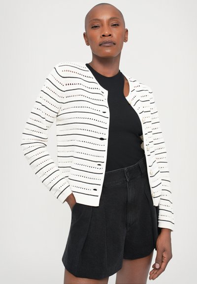 White knitted cardigan with horizontal black stripes, round neckline, and button closure, paired with high-waisted black shorts.