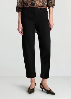 Pantalon noir taille haute à coupe décontractée avec ourlets retournés. Le tissu semble lisse avec une légère brillance, associé à des escarpins à bout pointu.