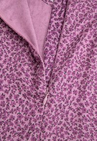 Fioletowa tkanina w kwiatowy wzór o gładkiej fakturze. Widać zamek błyskawiczny z metalowym suwakiem.