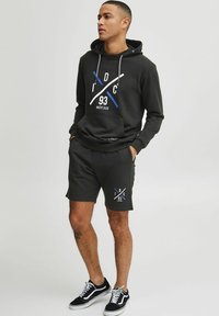 Sort bomulds-hoodie med hvide og blå grafik, parret med matchende sorte shorts med logo. Båret med sorte og hvide sneakers.