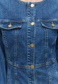 Farkkutakki keskipunaisena, jossa on muotoiltu suunnittelu, messinkiset napit, kaksi rintataskua ja näkyvät ompeluyksityiskohdat.