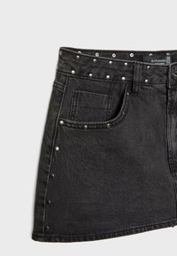 Jupe en denim noir avec des clous en métal argenté le long de la taille et de l'ourlet, dotée d'une poche avant et d'un design classique à cinq poches.