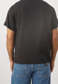 Czarna bawełniana koszulka z krótkim rękawem i luźnym krojem, w zestawieniu z niebieskimi dżinsami z tylnymi kieszeniami oraz metką z logo.