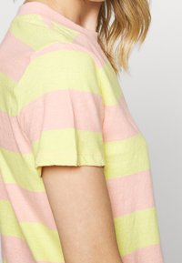 Camiseta de rayas en rosa y amarillo, hecha de algodón. Presenta un escote redondo y mangas cortas, con dobladillo cosido y un corte cómodo.