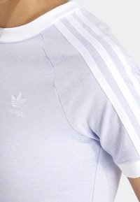 Light purple athletic t-shirt featuring white stripes on the shoulders, ribbed white collar, and embroidered logo on the chest.