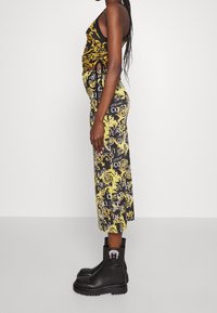 Svart linne med gul barockmönster, kombinerat med en svart kjol med vit text och gula detaljer, kompletterat med klumpiga svarta stövlar.