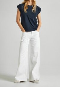 Tmavě modré tričko s krátkým rukávem, volný střih, ve spojení s bílými širokými kalhotami. Oblečení má ležérní, moderní design.