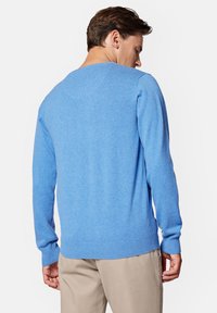 Niebieski sweter z dzianiny z długimi rękawami, ribbowanym dołem i mankietami. Posiada szeroki dekolt oraz gładką, miękką fakturę. Noszony z jasnymi spodniami.