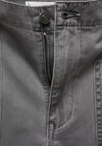 Pantalons en denim gris avec fermeture éclair à l'avant et bouton, présentant des coutures visibles et une texture lisse, mettant en avant des détails de design pratiques.