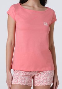 T-shirt di cotone rosa chiaro con scollo rotondo e maniche corte, abbinata a pantaloni corti rosa con motivi floreali bianchi piccoli.