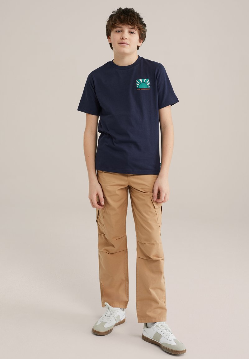 Marineblauwe t-shirt met korte mouwen en een kleurrijk grafisch zakontwerp, gecombineerd met beige cargobroek met zijzakken en witte sneakers.