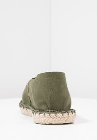 Olive green canvas espadrille with a textured rubber sole, featuring a braided jute edge and minimal stitching accents.