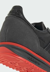 Baskets noires avec dessus en daim, semelle en caoutchouc rouge et accents texturés. Comprend un talon moulé avec un détail de logo en relief.