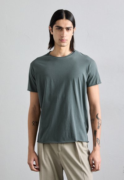 Σκούρο πράσινο βαμβακερό t-shirt με κοντά μανίκια και στρογγυλή λαιμόκοψη, διαθέτοντας χαλαρή γραμμή. Λείο ύφασμα, ίσιες ραφές και διακριτές λεπτομέρειες ραφής.